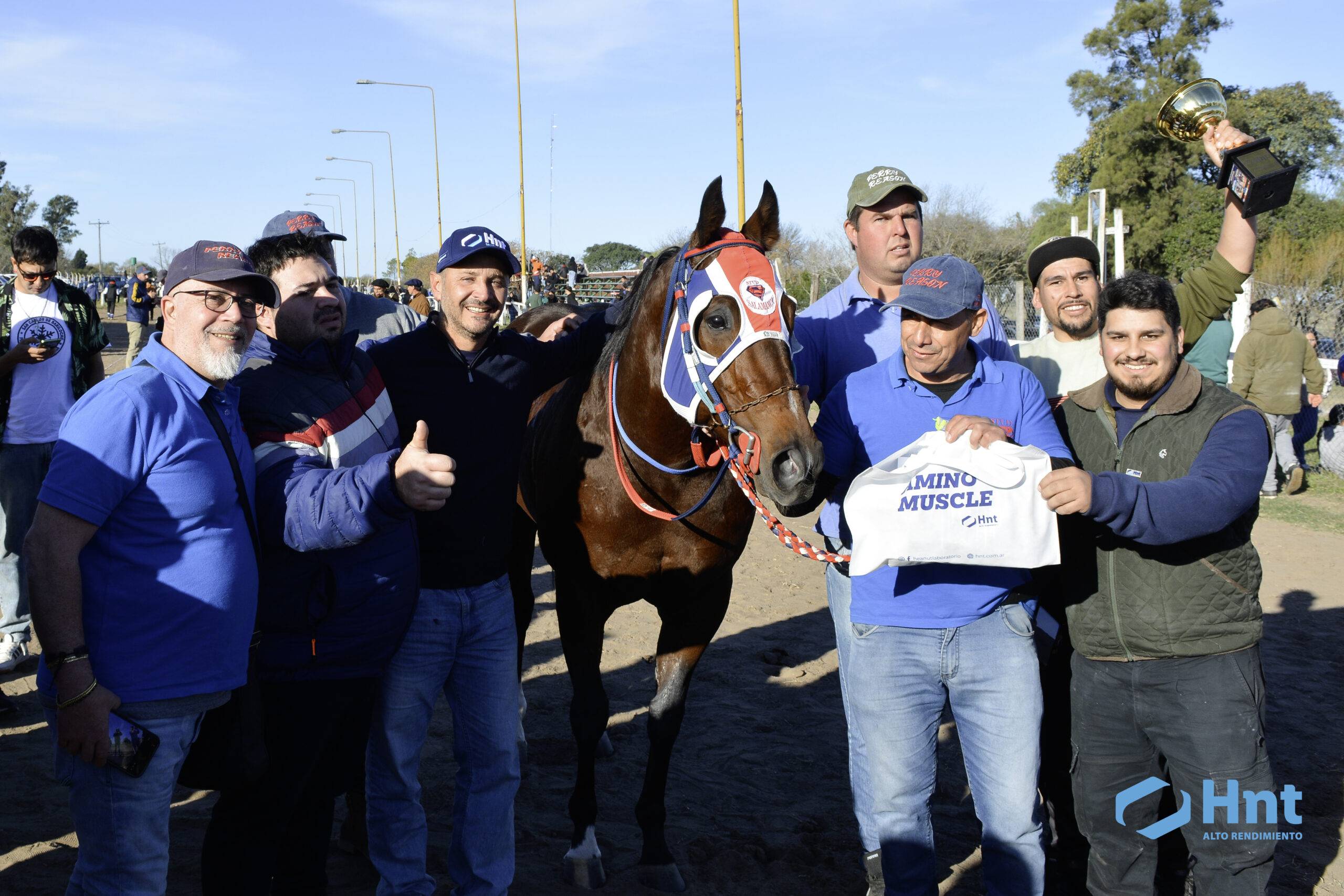 Perry Reason y el Stud Salamanca celebran la victoria en la Mega Clásico Laboratorio HNT con la copa y el banner AminoMuscle