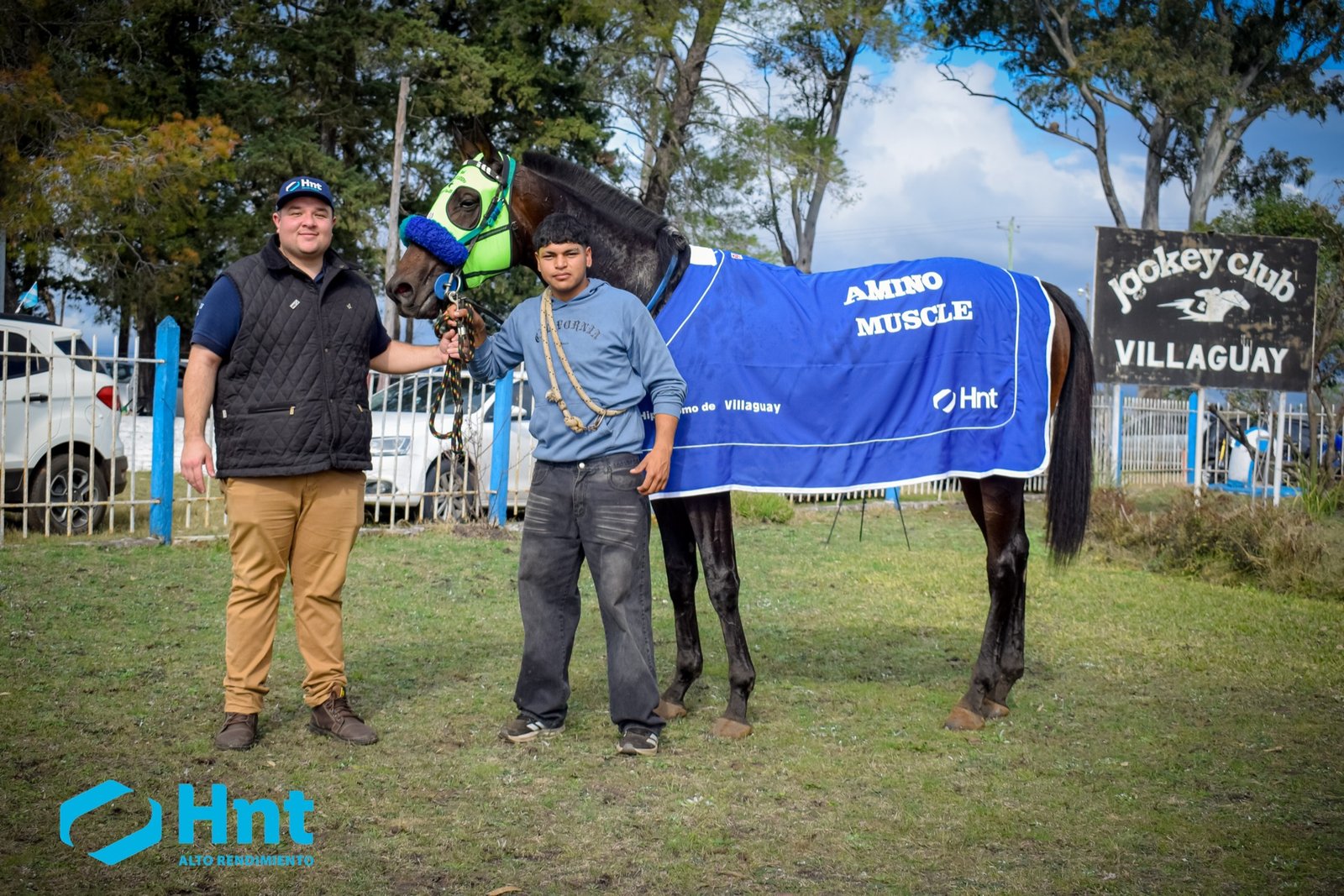 Avivador posando con la manta AminoMuscle del Laboratorio HNT junto al cartel del Jockey Club Villaguay