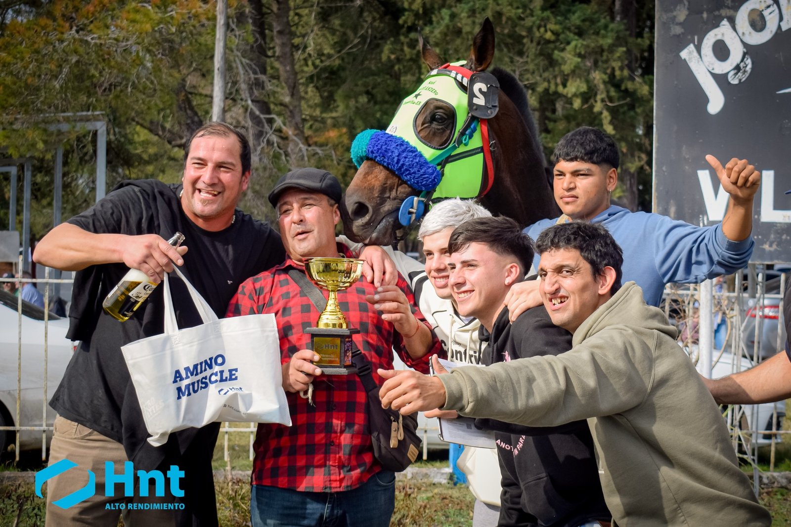 Cuidadores y allegados de Avivador celebrando con la copa dorada y el bolso AminoMuscle del Laboratorio HNT