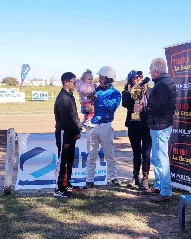 Leandro Depetris recibe el trofeo de la Copa HNT Las Varillas junto a su familia frente al banner del Laboratorio HNT