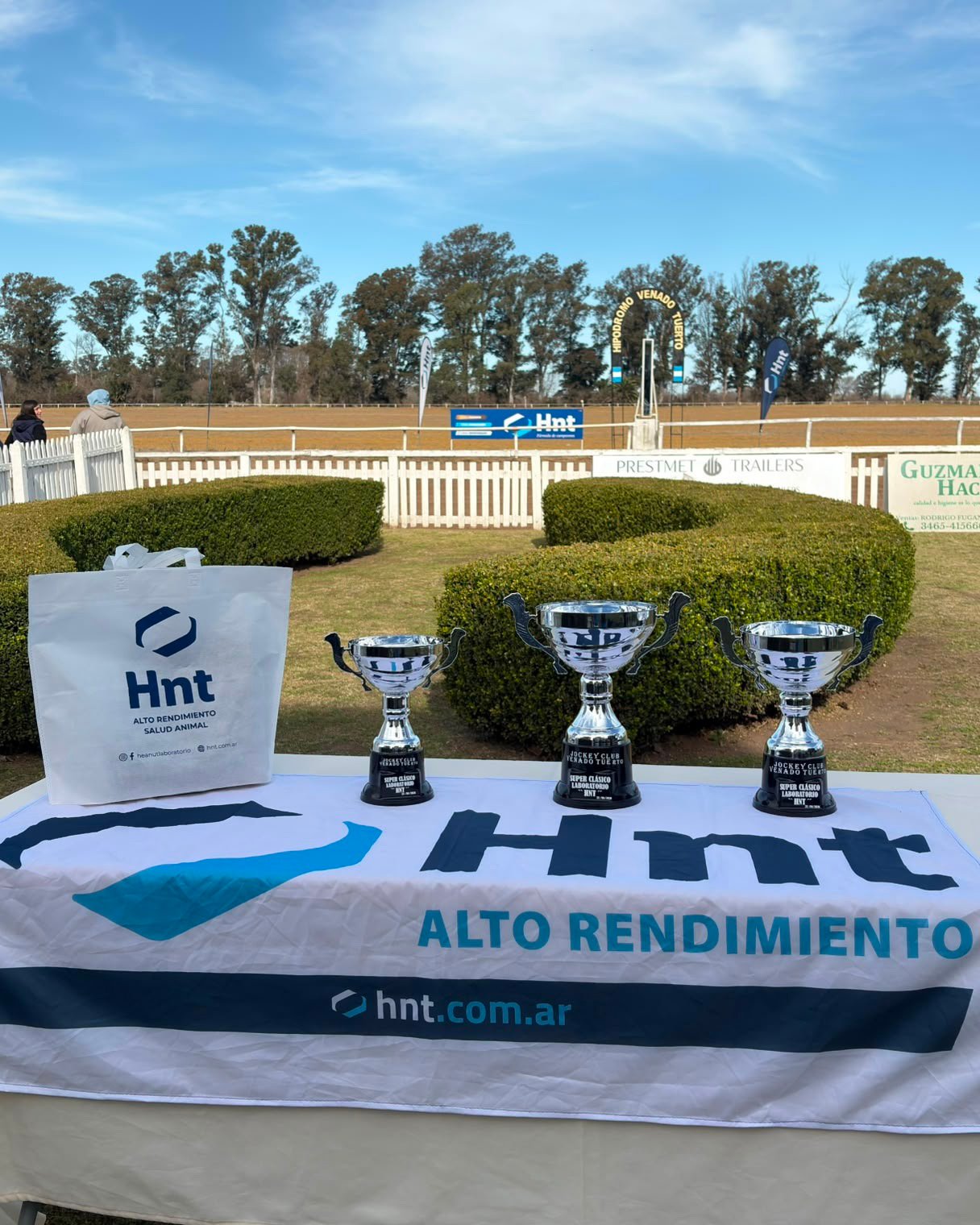 Los tres trofeos del Súper Clásico Laboratorio HNT sobre la mesa del Jockey Club Venado Tuerto con la pista de fondo