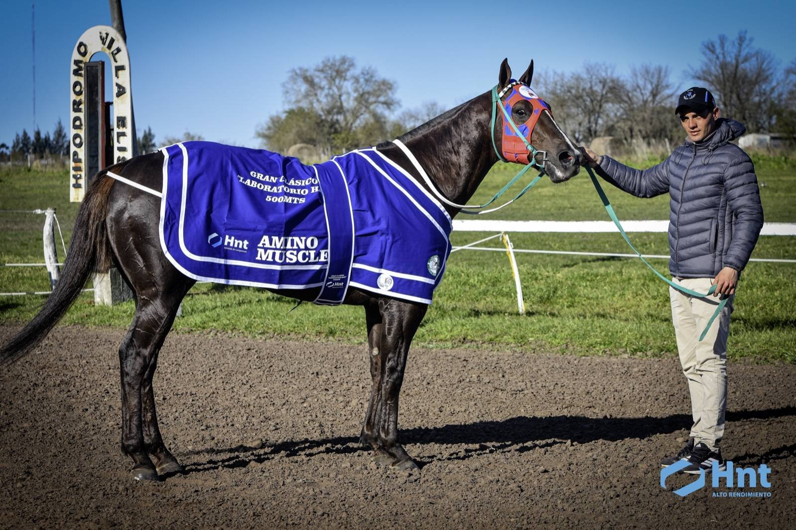 Comanche con la manta del Gran Clásico Laboratorio HNT en el Hipódromo de Villa Elisa junto a su cuidador